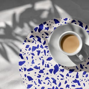 Könnte beinhalten: Ein runder Untersetzer aus weißem und blauem Terrazzo mit einer weißen Untertasse und einer weißen Tasse Kaffee darauf.