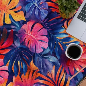 Może przedstawiać: Laptop, notes, słuchawki i filiżanka kawy ułożone na kolorowej powierzchni z tropikalnym wzorem liści.