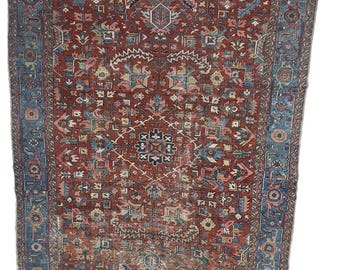 May include: A rectangular, antique rug with an intricate, geometric pattern. The rug features a central field of deep red with a complex design in shades of blue, pink, and cream. A blue border frames the rug, adding contrast and definition. The rug appears to be well-worn.