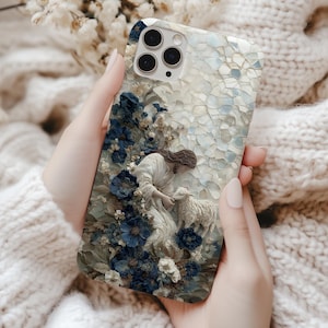 May include: A phone case featuring a religious scene with a figure in white robes and a lamb, surrounded by blue flowers. The case has a mosaic-like background and is held by a person wearing a white sweater.