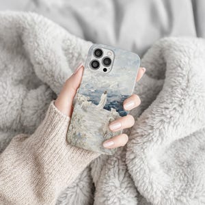 May include: A phone case featuring an impressionistic painting of a person standing on a cliff overlooking the ocean. The artwork is in shades of blue, white, and gray, with a textured, painterly effect. The case has a glossy finish and a camera cutout.