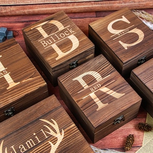 May include: A collection of wooden boxes with engraved initials and names. The boxes are various sizes and feature dark brown wood with metal clasps. Some boxes have a single initial, while others have a name.