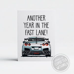 May include: A white car with a black spoiler and red taillights. The car has the text "GTR" on the back. The text "Another year in the fast lane!" is above the car. The text "Designed by Cupoftea withmilk" is below the car.