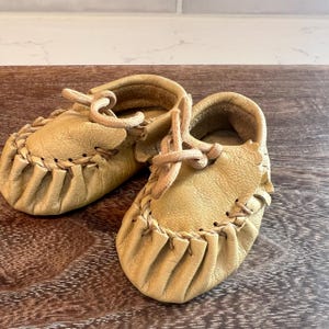 May include: A white ceramic mug with a black handle and the text "But First, Coffee" in a black, handwritten-style font. The mug is on a white surface.