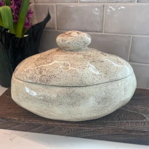 May include: A set of three ceramic mugs with a speckled, matte finish. The mugs are in shades of cream, light gray, and dark gray. Each mug has a simple, minimalist design, perfect for coffee or tea.