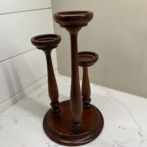 May include: A wooden candle holder with three candle cups. The holder is dark brown and has a round base.
