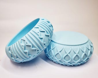 Puede incluir: Dos cuencos de cerámica azul claro con patrones decorativos en relieve. El cuenco de la izquierda tiene un patrón geométrico y el cuenco de la derecha tiene un patrón más intrincado.