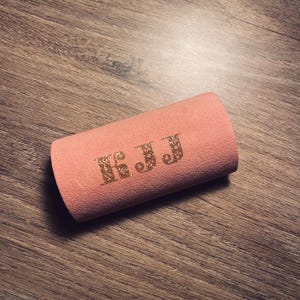 May include: A pink fabric tube with the letters "K.J.J" in gold glitter.