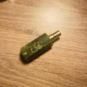 Puede incluir: Una botella de vidrio verde con una boquilla de pulverización dorada y la palabra "ESE" escrita en el lateral.