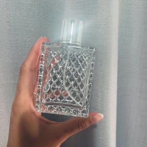 Op de afbeelding: Een doorzichtige glazen fles met een zilveren spuitmond en een textuurontwerp. De fles is gelabeld met de tekst "My Chanel Perfume".