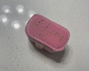 May include: A small pink velvet ring box with a gold inscription that reads "Vera".