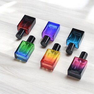 May include: Six small glass bottles with black spray tops. The bottles are filled with colorful liquids that create a rainbow effect. The bottles are arranged in a row on a light wood surface.