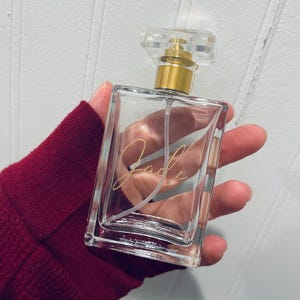 May include: A clear glass bottle with a gold spray nozzle and a gold inscription that reads "Jade".