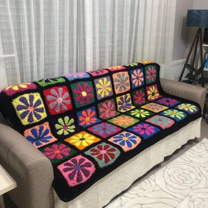 May include: A colourful crocheted throw blanket with a black background and a floral pattern. The blanket is draped over a sofa.