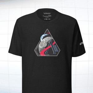 May include: Black t-shirt featuring a triangular graphic with a moon, Earth, and a stylized letter "A". The graphic includes the names WISEMAN, GLOVER, KOCH, and HANSEN. The word "ARTEMIS" is printed on the sleeve. The shirt also has the text "DIGITAL ASTRONAUT".