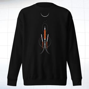 May include: Black sweatshirt featuring a minimalist graphic of rockets launching into space. The design includes orange and white rockets with stylized trails, a crescent moon, and stars. The sweatshirt is a crew neck style.