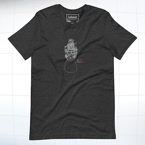 May include: A dark heather grey t-shirt featuring a white outline of a rocket engine. The text "DIGITAL ASTRONAUT" is printed on the shirt.