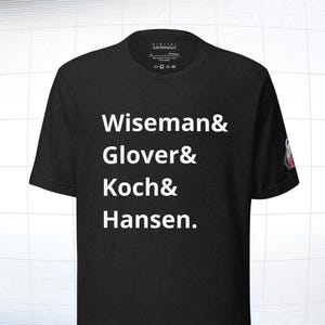 Może przedstawiać: Czarny t-shirt z okrągłym dekoltem z białym tekstem: Wiseman & Glover & Koch & Hansen. Koszulka ma małe logo na rękawie i metkę na dekolcie z napisem "DIGITAL ASTRONAUT".