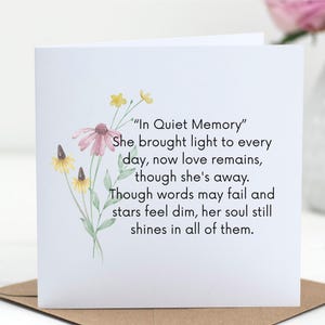 Pode incluir: Cartão branco com o texto "In Quiet Memory" e um design floral em aquarela. O cartão apresenta uma flor-de-cone rosa e flores amarelas. O cartão está em um envelope marrom.