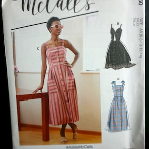 May include: McCall's M7950 sewing pattern envelope featuring a sleeveless button-front dress with pockets in a red and white striped fabric. The envelope displays illustrations of two additional dress variations, one black and one blue plaid.
