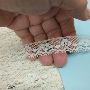 May include: White lace trim with a delicate floral pattern. The trim is approximately 1 inch wide and has a scalloped edge.