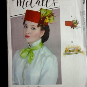 May include: McCall's sewing pattern featuring a woman wearing a red hat with green and yellow floral accents. The pattern includes illustrations of the hat and other designs. The text "Angela Clayton" is visible.