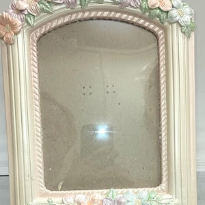 May include: A white picture frame with a pink and green floral design. The frame has a rope-like border and a clear glass insert.