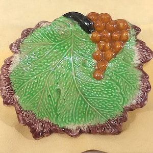May include: A green ceramic leaf-shaped dish with a raised design and a cluster of brown grapes on top.