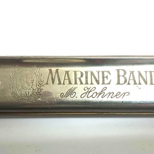 May include: A silver harmonica with a brass casing. The harmonica is labeled "Marine Band M. Hohner".