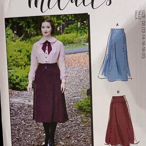 May include: McCall's sewing pattern M8071 featuring a woman in a pink blouse and burgundy skirt. The pattern includes illustrations of a blue skirt and a burgundy skirt. The text "Angela Clayton" is visible.