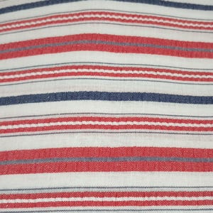 May include: Close-up of a fabric with a repeating pattern of horizontal stripes. The stripes alternate between red, white, and navy blue. The fabric appears to be woven, with a slightly textured surface. The overall effect is a classic, nautical or patriotic design.