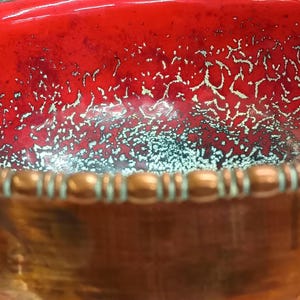 May include: A large copper bowl with a red interior and a decorative copper rim. The interior of the bowl has a speckled, metallic finish.