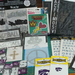 May include: A collection of craft supplies including glitter transfer shapes, iron-on letters, patches, and rhinestone designs. The items feature various colors, shapes, and text, suitable for DIY projects and apparel customization.
