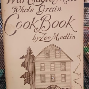 May include: A vintage cookbook titled "War Eagle Mill Whole Grain Cookbook by Zoe Medlin". The cover features a brown illustration of a watermill with a water wheel.