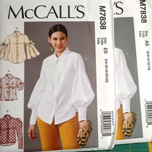 May include: Two white paper sewing pattern envelopes for McCall's M7838, featuring illustrations of button-down shirts with various sleeve styles, including long puff sleeves and flared sleeves, with size ranges E5 and A5 printed on the front.