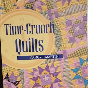 May include: Book cover with a yellow, purple, and pink patchwork quilt design. The title is "Time-Crunch Quilts" by Nancy J. Martin. A clock face is partially visible in the upper left corner. The text "FREE bonus CD-ROM inside!" is in the lower right corner.