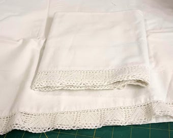Puede incluir: Un juego de ropa de cama blanca con una base de tela lisa y sólida y un borde decorativo de encaje de ganchillo a lo largo del extremo inferior. El juego incluye una sábana grande y una funda de almohada doblada, ambas con el mismo encaje.