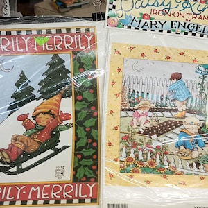 May include: Two iron-on transfers featuring illustrations. One shows a child sledding in a winter scene with the text "Merrily Merrily." The other depicts children in a garden with the text "Silentla...Heaven...Angels."