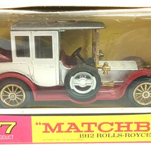 May include: A Matchbox Y-7 1912 Rolls-Royce toy car in its original box. The model car is white, red, and silver with gold-colored wheels. The box is pink and yellow with the Matchbox logo and car details.