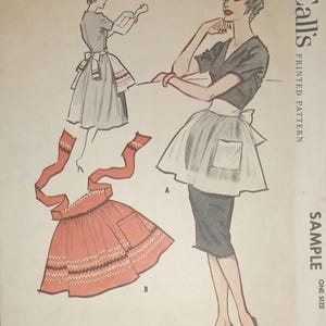 May include: Vintage McCall's sewing pattern for a short apron. The pattern is for a sample size and includes instructions for making the apron. The pattern shows two women wearing the apron, one in a red and white apron and the other in a white apron.
