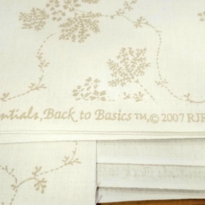 May include: Off-white fabric with a repeating pattern of beige floral sprigs and vines. The text "Base Essentials, Back to Basics TM, © 2007 RJR Fabrics" is printed across the fabric. The fabric is folded.
