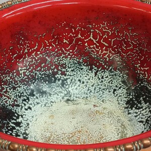 May include: A large, red copper bowl with a white and black crackled glaze. The bowl has a decorative copper rim.