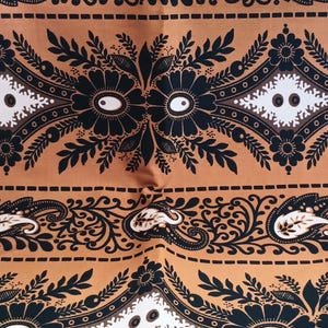 May include: Brown fabric with a black and white paisley pattern. The fabric has a repeating design of stylized flowers and leaves.