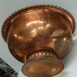 May include: A large copper bowl with a hammered finish and a decorative beaded rim. The bowl sits on a wide, round base.