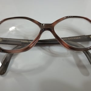 May include: Brown and tan eyeglasses with a unique octagonal frame shape. The arms and bridge are a translucent gray. The text "FRAME FRANCE" and "VAN-CHARGER" are visible on the frame. The lenses are clear.
