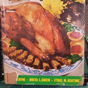 May include: A vintage cookbook titled "The Best From Midwest Kitchens" with a photo of a roasted turkey on the cover. The cookbook authors are listed as "Lothe, Breta L. Griem, Ethel M. Keating".