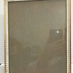 May include: A gold picture frame with a white inner border. The frame has a decorative pattern around the edge.