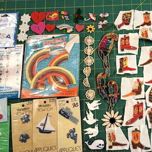 May include: A collection of craft supplies including iron-on patches, sew-on appliques, and buttons. The patches feature rainbows, cowboy boots, and birds. The appliques include a sailboat and a dancer. The buttons are heart-shaped.