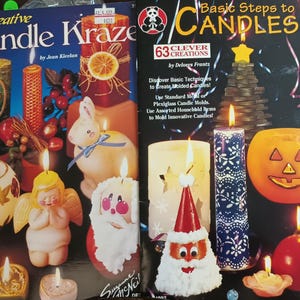 May include: Two books on candle making, "Creative Candle Kraze" and "Basic Steps to Candles", are displayed. The covers showcase various candle projects, including heart-shaped, angel, and Santa Claus designs. The books offer instructions for creating unique candles.