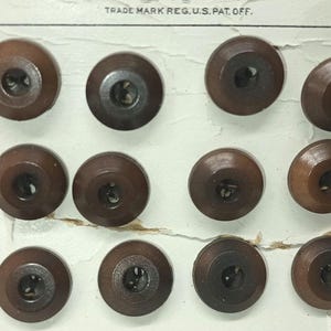 May include: A card with 12 brown wooden buttons arranged in rows. The buttons have a raised center and a smooth, polished finish. The card has the text "TRADE MARK REG. U.S. PAT. OFF." printed on it.
